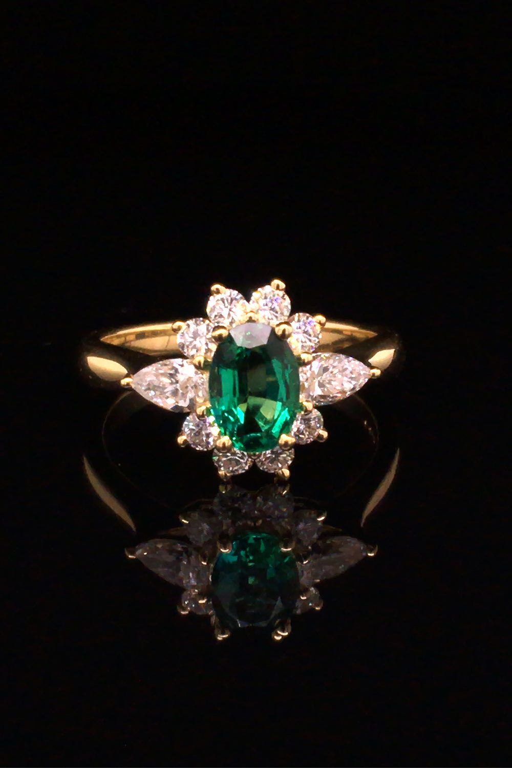 18K gold ring featuring an oval emerald with diamonds on a black background