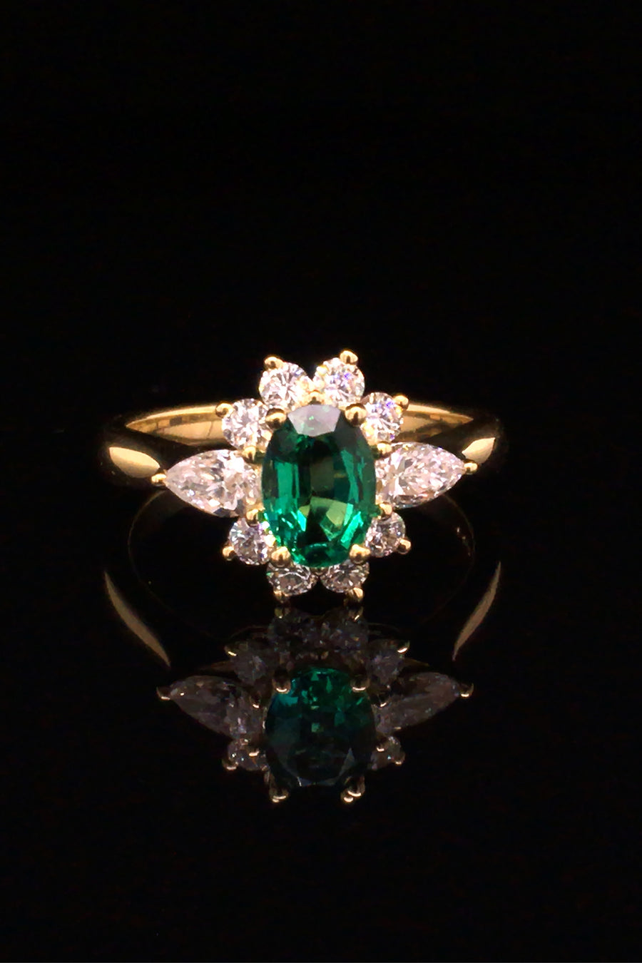 18K gold ring featuring an oval emerald with diamonds on a black background