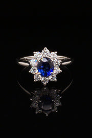 Platinum ring with oval blue sapphire surrounded by brilliant diamonds on black background.