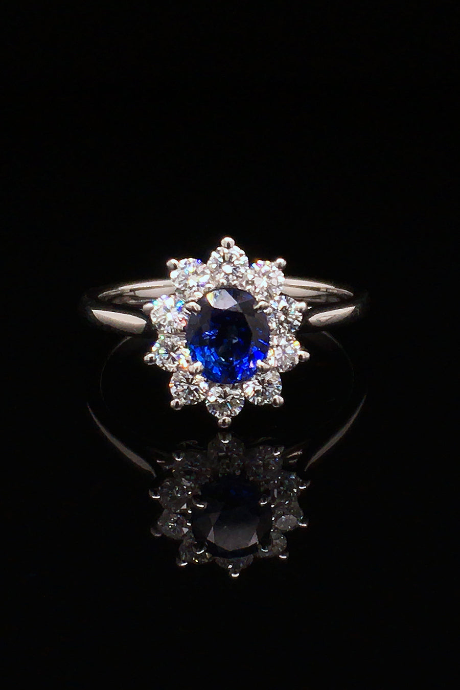 Platinum ring with oval blue sapphire surrounded by brilliant diamonds on black background.