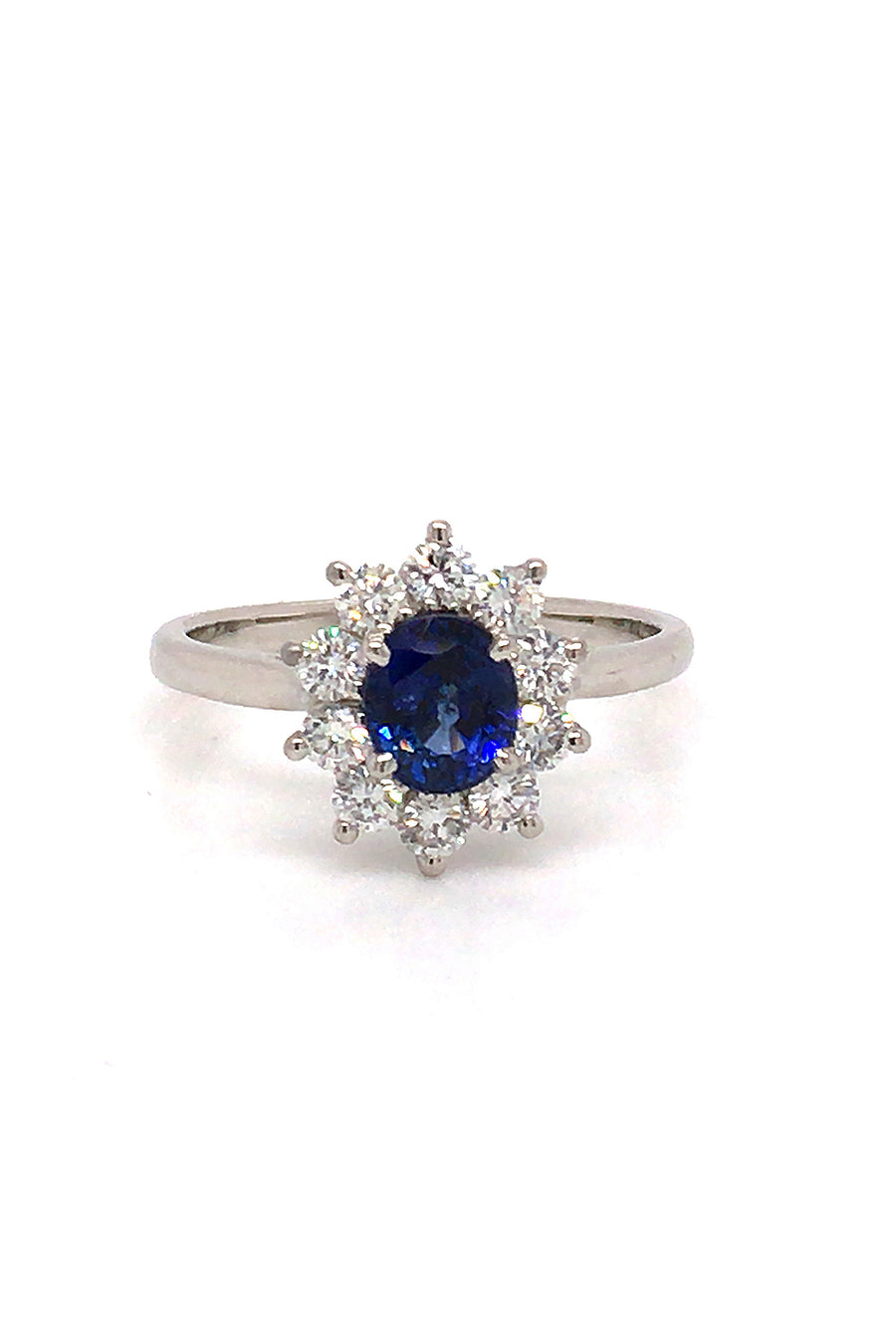 Platinum ring with oval blue sapphire surrounded by brilliant diamonds on white background.