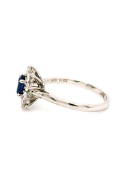 Side view of platinum ring with oval blue sapphire surrounded by brilliant diamonds on white background.