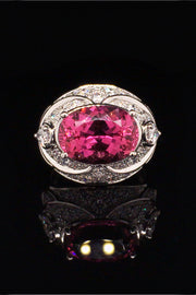 Platinum ring with an oval rubellite, two pear-shaped diamonds, and brilliant diamonds on a black background.