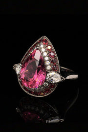 Angle view of 18K white gold ring with a pear-shape rubellite surrounded by diamonds and rubies with a black rhodium finish on a black background