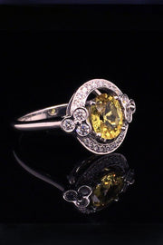 Angle view of an 18K white gold ring with a yellow sapphire and lace motif with diamonds on a black background