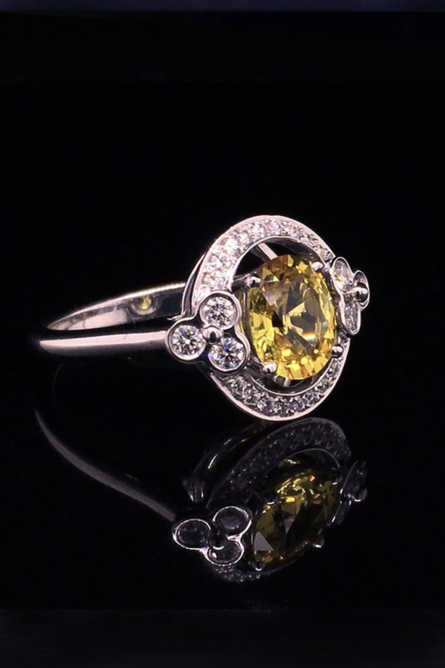 Angle view of an 18K white gold ring with a yellow sapphire and lace motif with diamonds on a black background