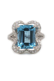 18K white gold ring with an emerald-cut aquamarine and diamonds in a ribbon motif on a white background