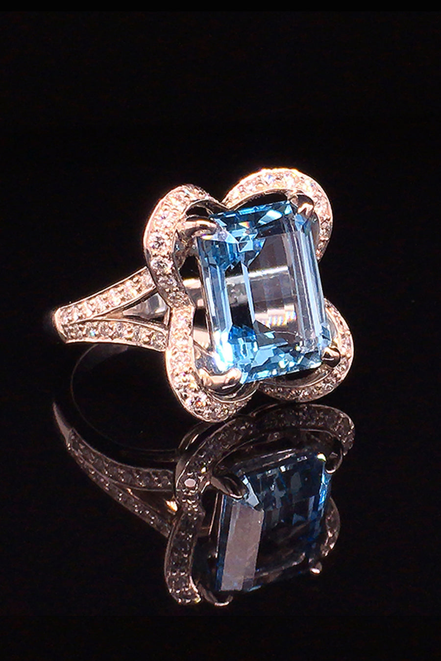 Angle view of 18K white gold ring with an emerald-cut aquamarine and diamonds in a ribbon motif on a black background