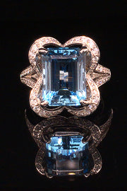 18K white gold ring with an emerald-cut aquamarine and diamonds in a ribbon motif on a black background