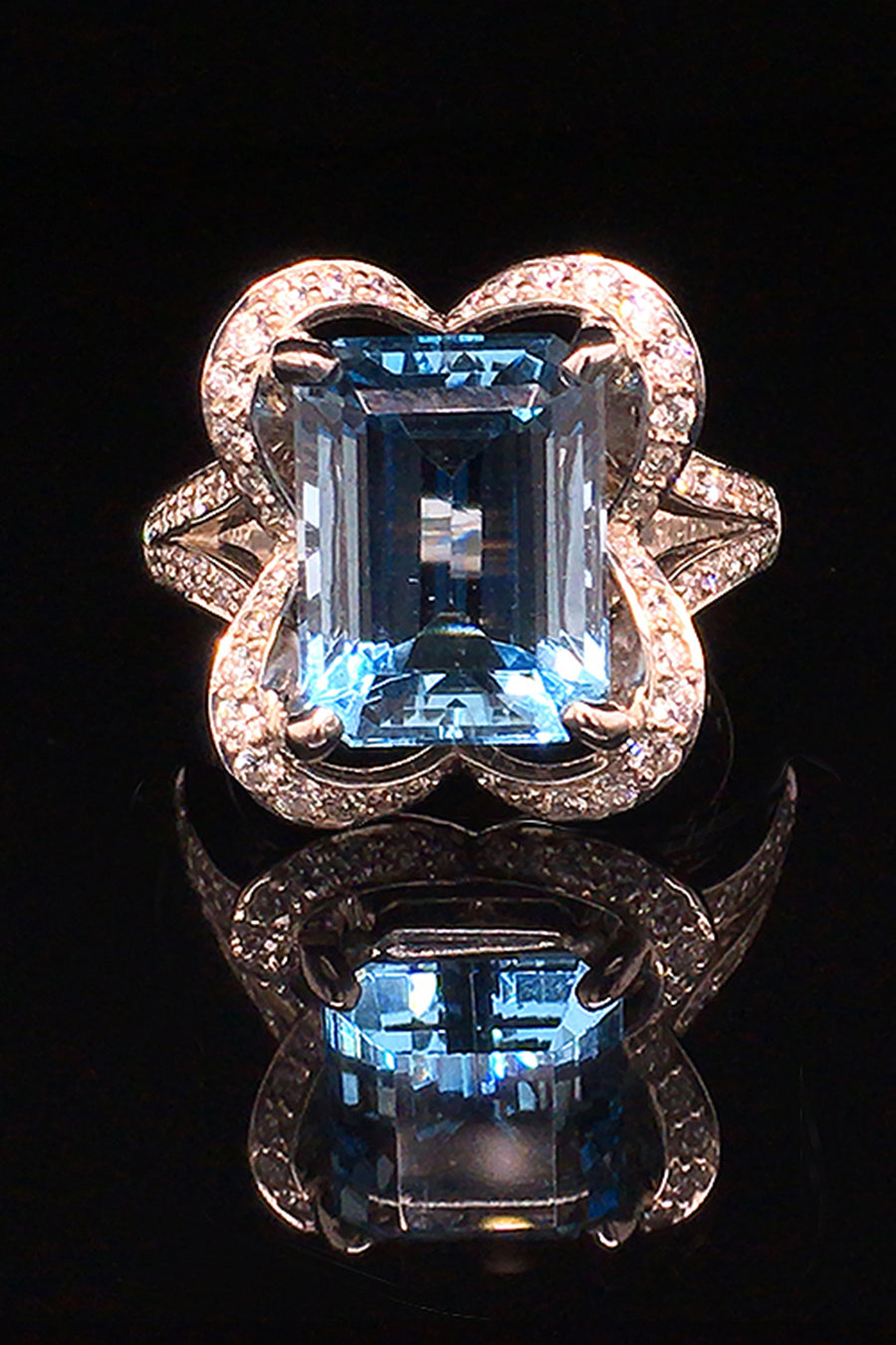 18K white gold ring with an emerald-cut aquamarine and diamonds in a ribbon motif on a black background