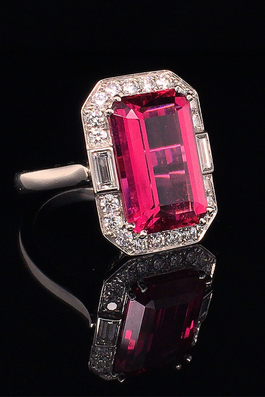 Angle view of a platinum ring with a large emerald-cut rubellite with baguette and brilliant diamonds on a black background