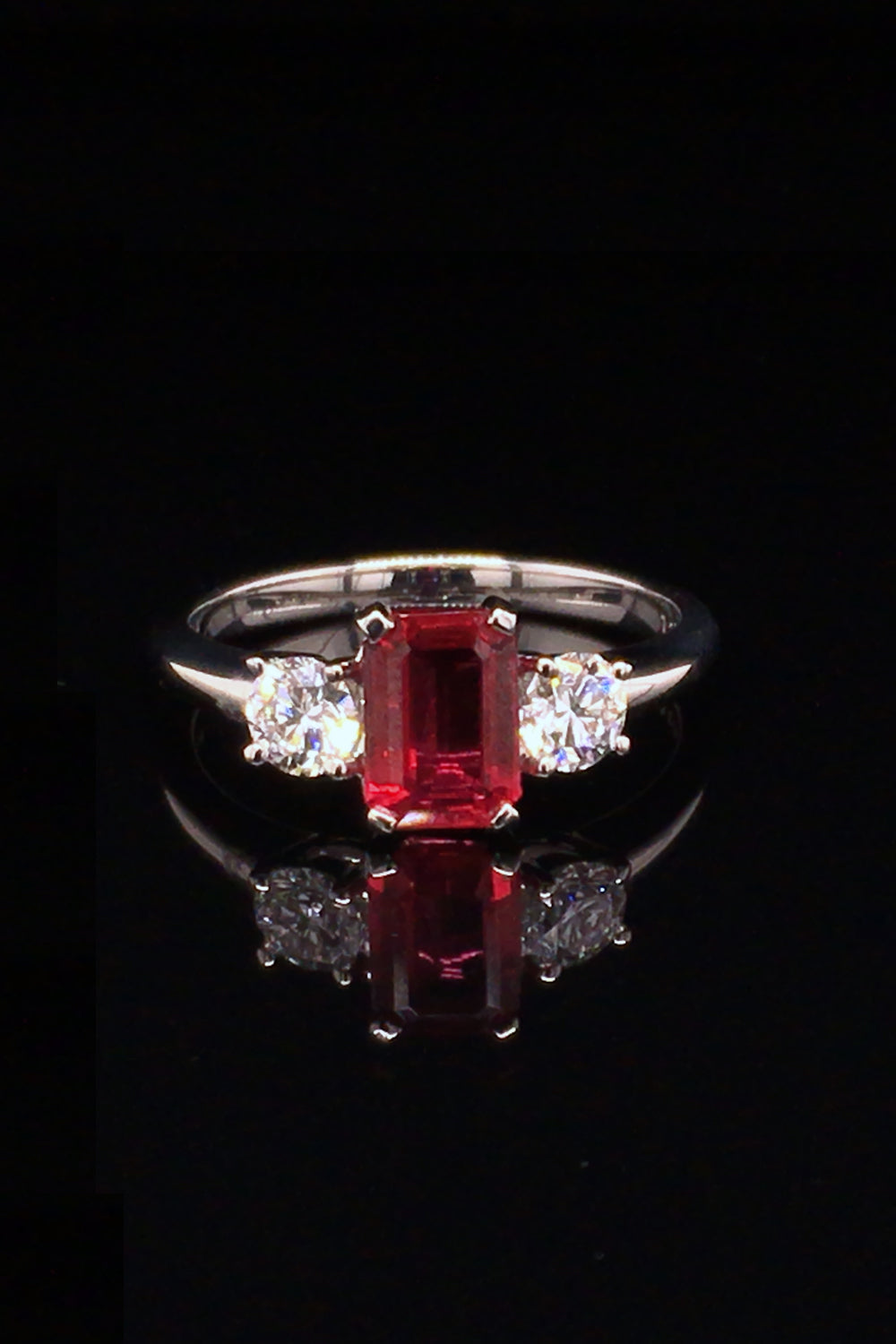 Platinum ring with an emerald-cut ruby and two round diamonds on a black background.