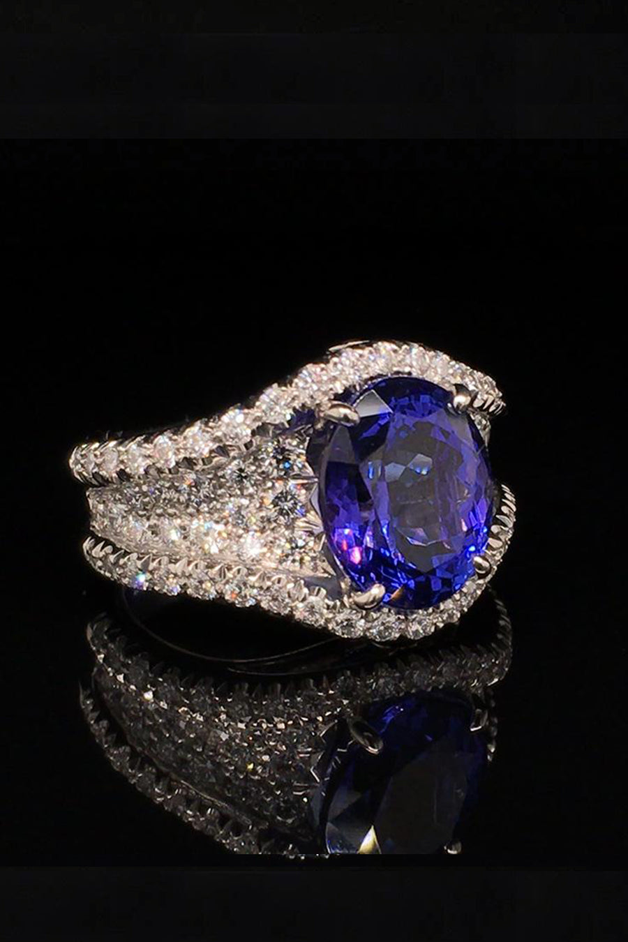 Angle view of platinum ring with an oval tanzanite and diamond pave on a black background