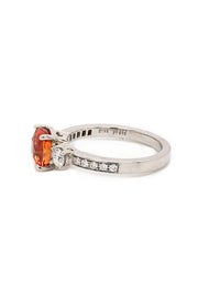 Side view of cushion-cut orange sapphire ring with diamonds in platinum on white background