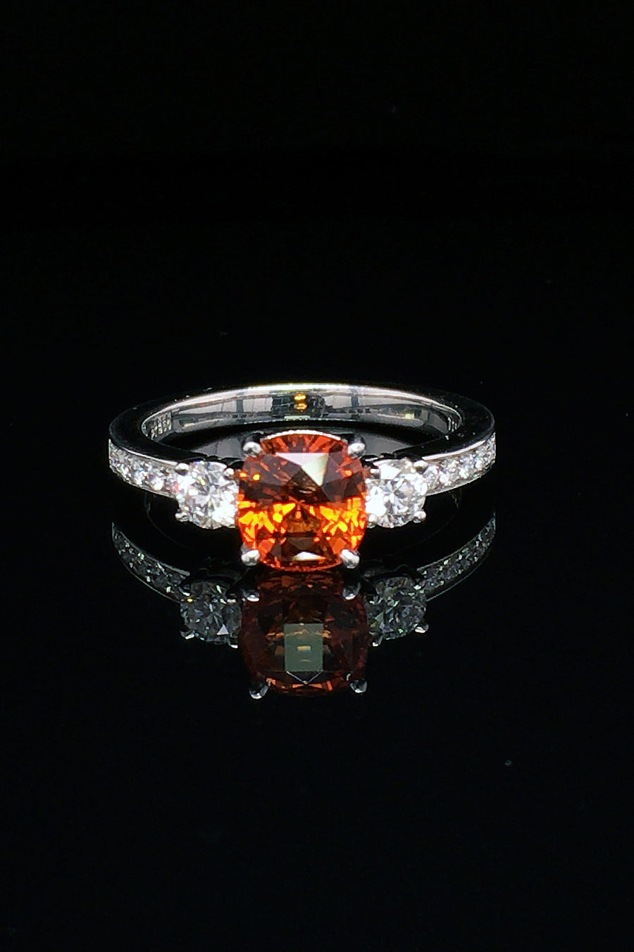 Cushion-cut orange sapphire ring with diamonds in platinum on black background
