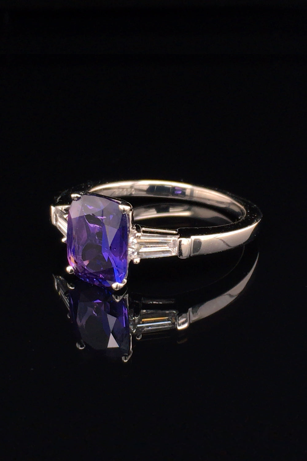 Angle view of platinum ring with purple blue color-change sapphire and tapered baguette diamonds on black background