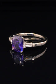 Angle view of platinum ring with purple blue color-change sapphire and tapered baguette diamonds on black background
