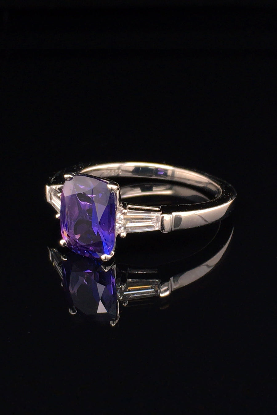 Angle view of platinum ring with purple blue color-change sapphire and tapered baguette diamonds on black background