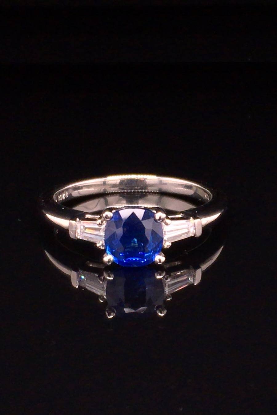 A platinum three-stone sapphire ring with tapered baguettes on black background.