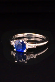 Angle view of platinum three-stone sapphire ring with tapered baguettes on black background.