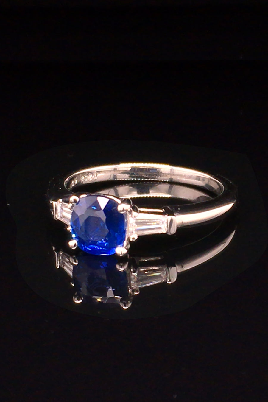 Angle view of platinum three-stone sapphire ring with tapered baguettes on black background.