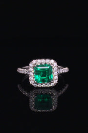 Platinum ring with emerald and diamond halo on black background.