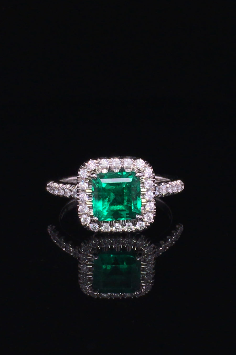 Platinum ring with emerald and diamond halo on black background.