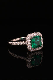 Angle of platinum ring with emerald and diamond halo on black background.