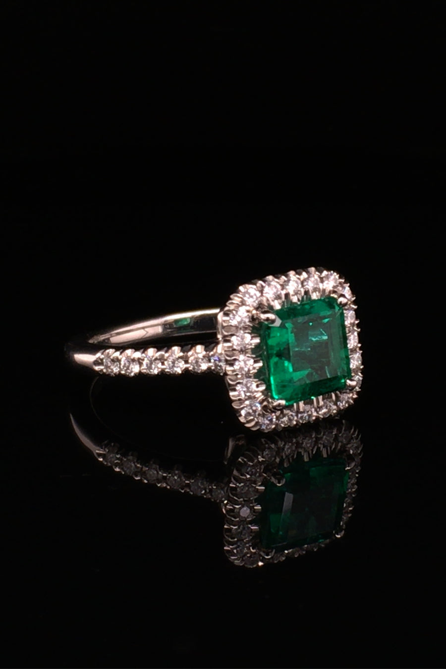 Angle of platinum ring with emerald and diamond halo on black background.
