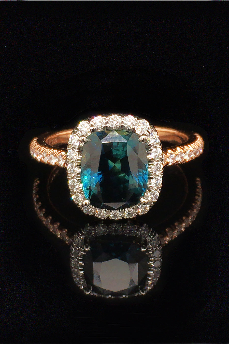 20K pink gold ring with a cushion-cut teal sapphire and diamond halo on a black background.