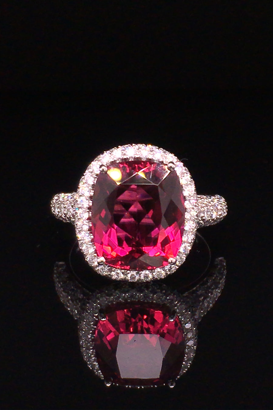 Platinum ring with a cushion rubellite and  diamond pave on a black background.