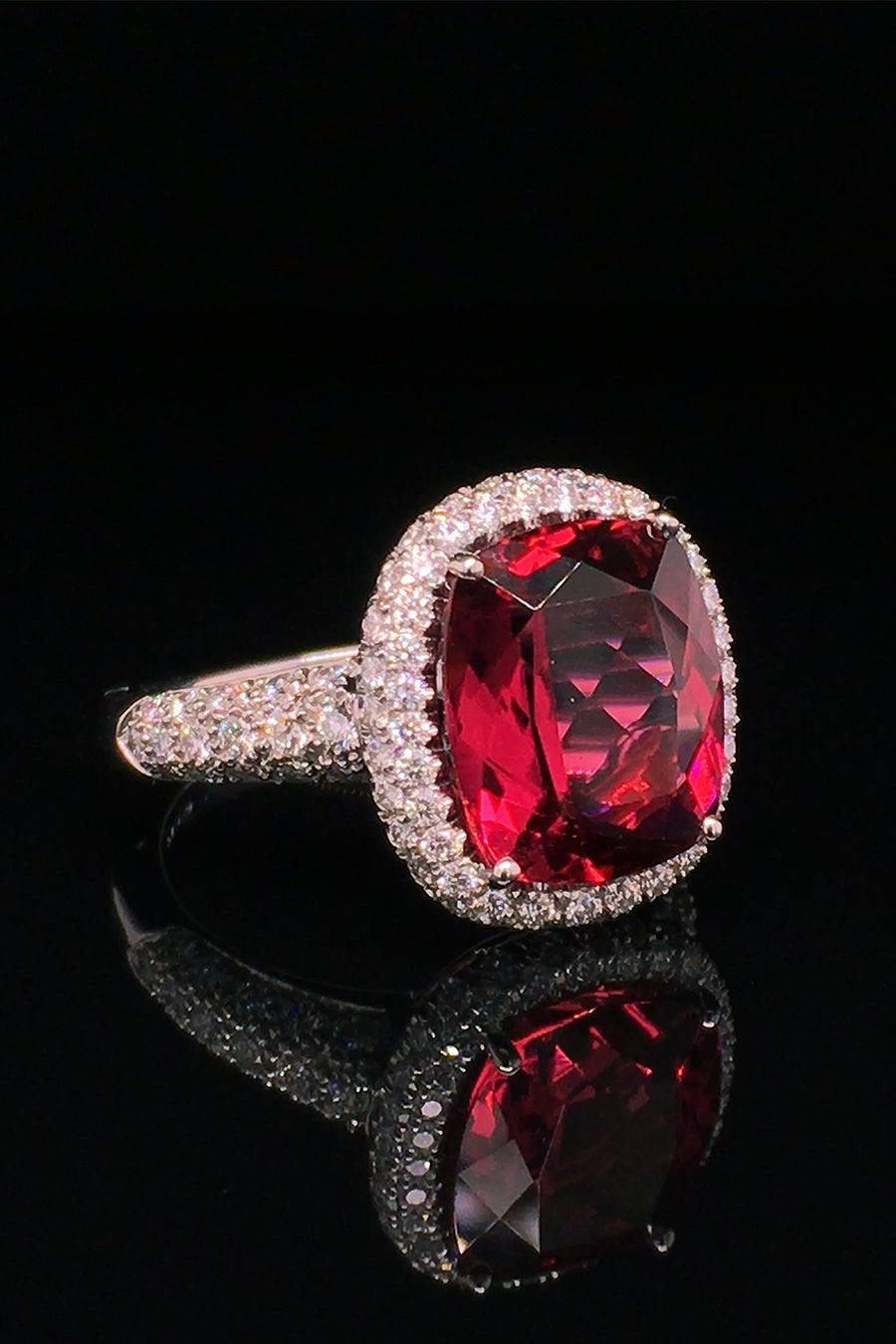 Angle view o platinum ring with a cushion rubellite and  diamond pave on a black background.