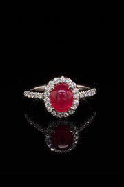 Platinum ring with a ruby cabochon and diamond halo on a black background.