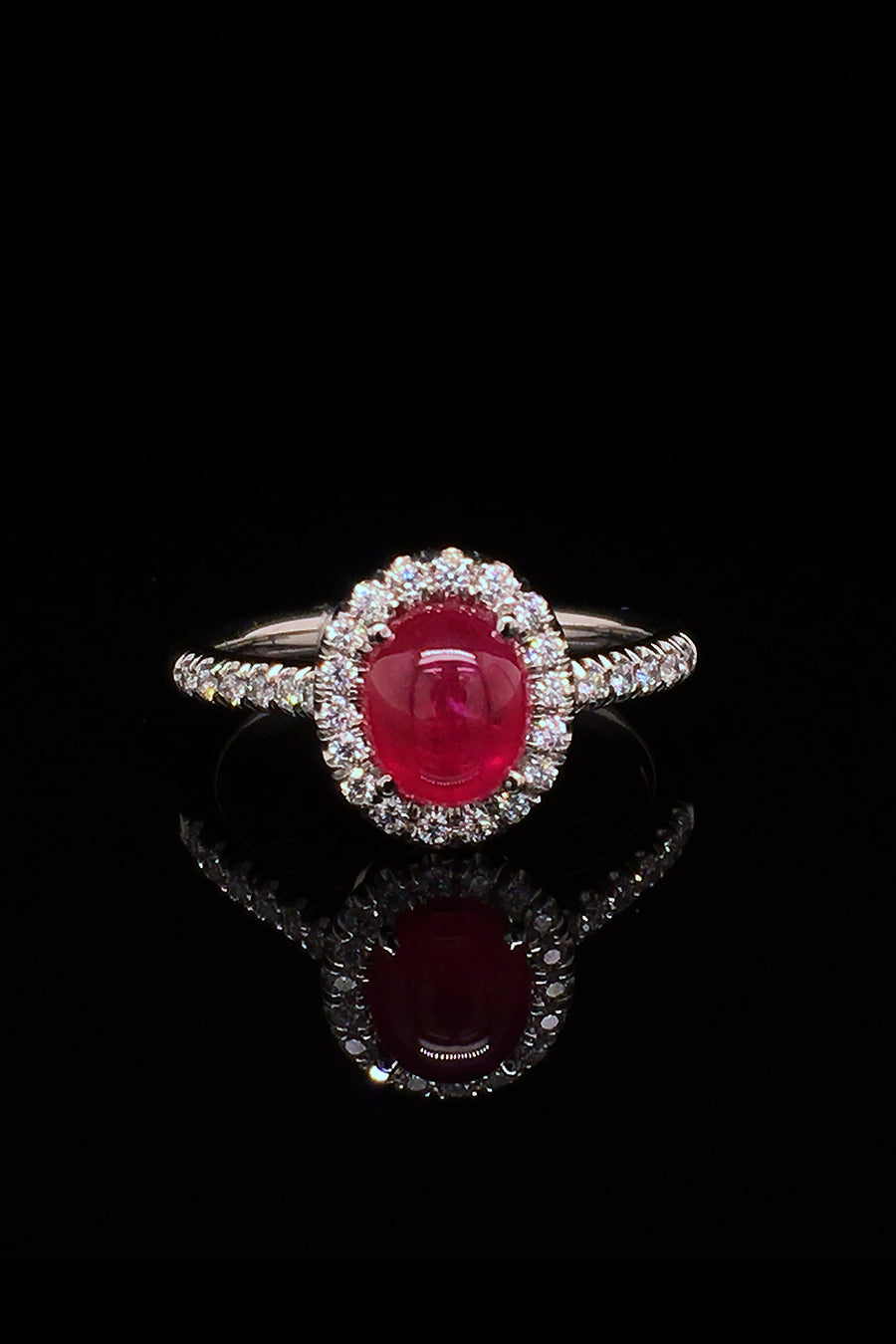 Platinum ring with a ruby cabochon and diamond halo on a black background.