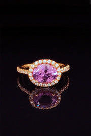 Side view of 20K pink gold ring with pink sapphire and diamond halo on black background