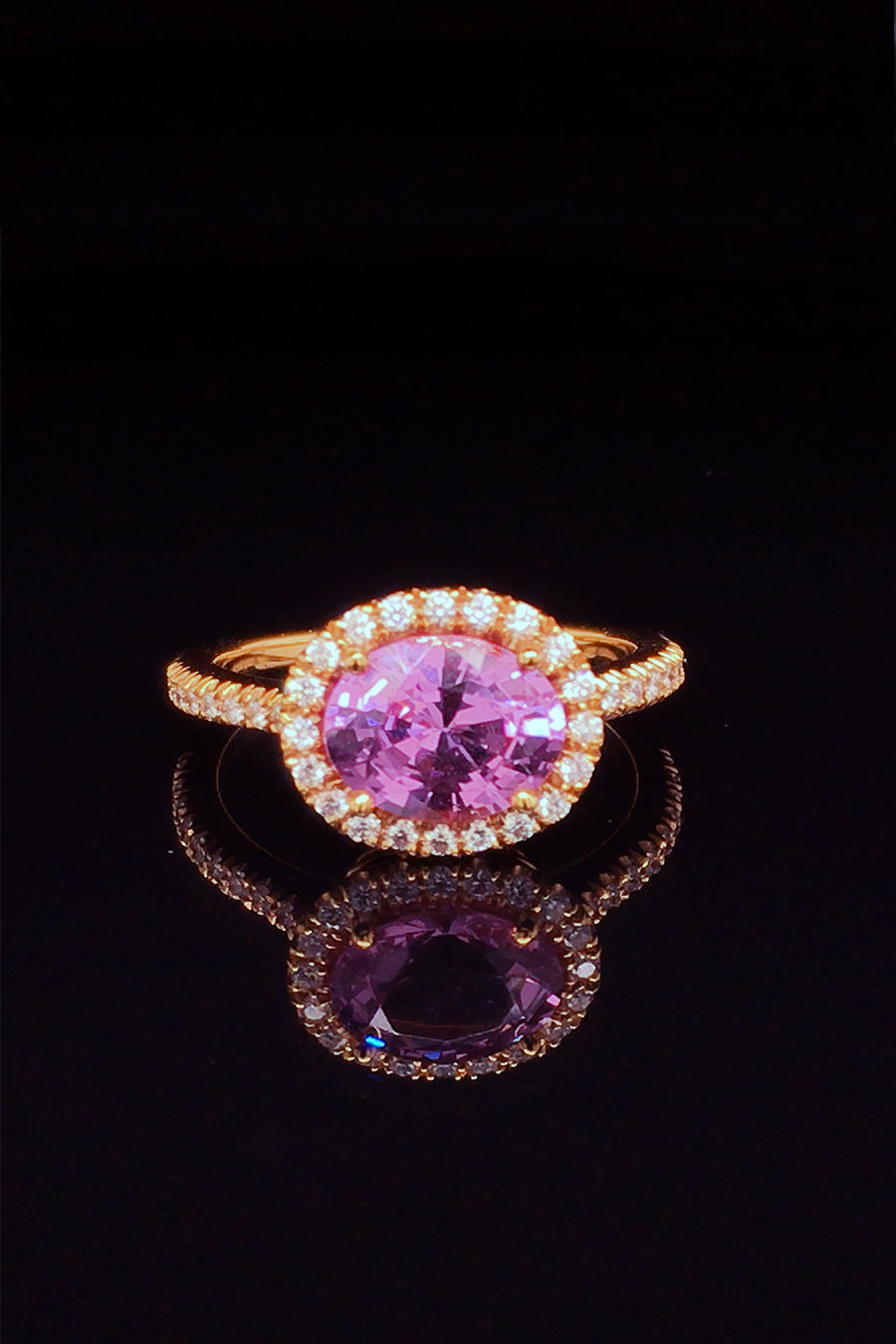 Side view of 20K pink gold ring with pink sapphire and diamond halo on black background