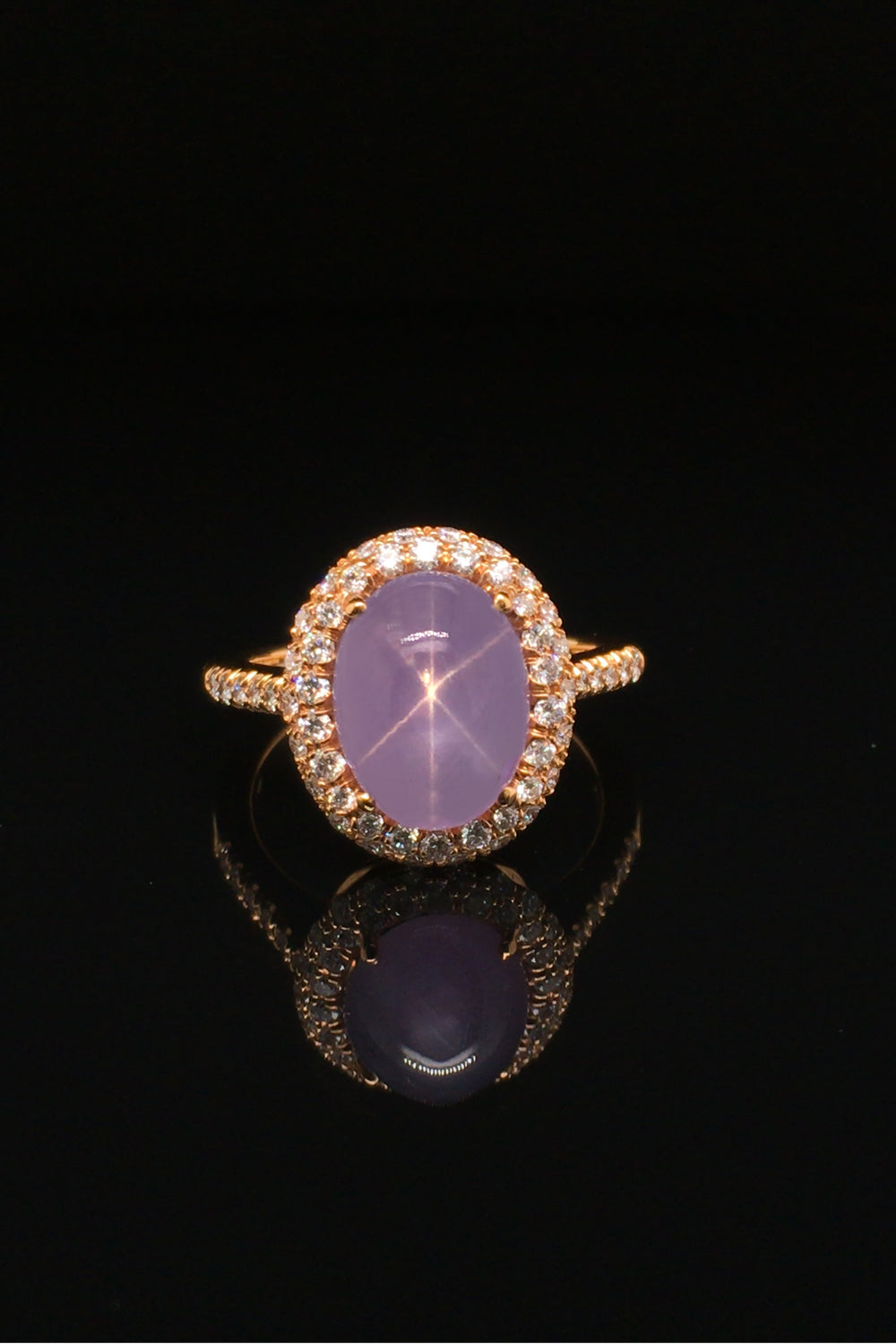 Lavender star sapphire ring with a diamond halo in 20K pink gold on a black background.