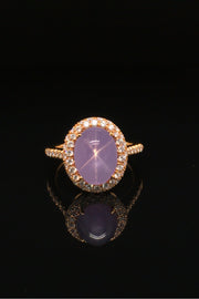 Lavender star sapphire ring with a diamond halo in 20K pink gold on a black background.
