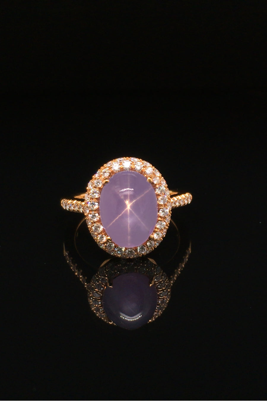 Lavender star sapphire ring with a diamond halo in 20K pink gold on a black background.