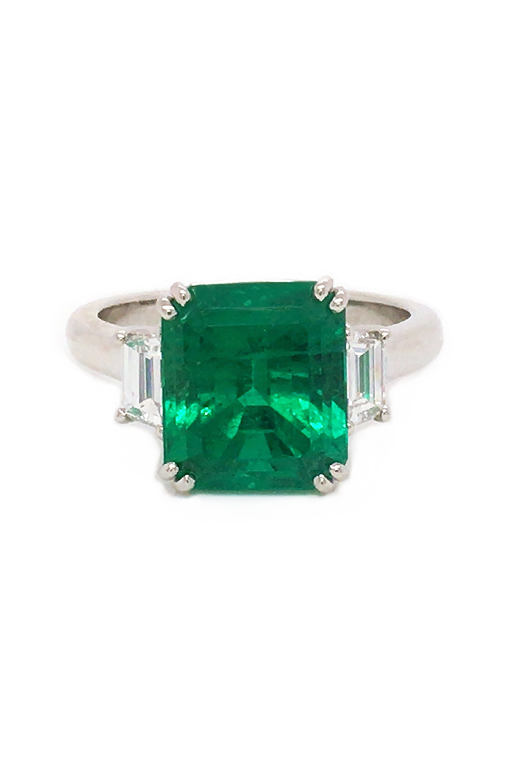 Platinum ring with an emerald and trapezoid diamonds on a white background