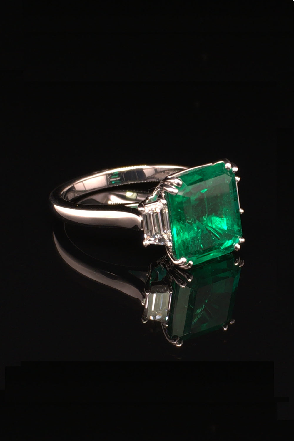 Side view of platinum ring with an emerald and trapezoid diamonds on a black background