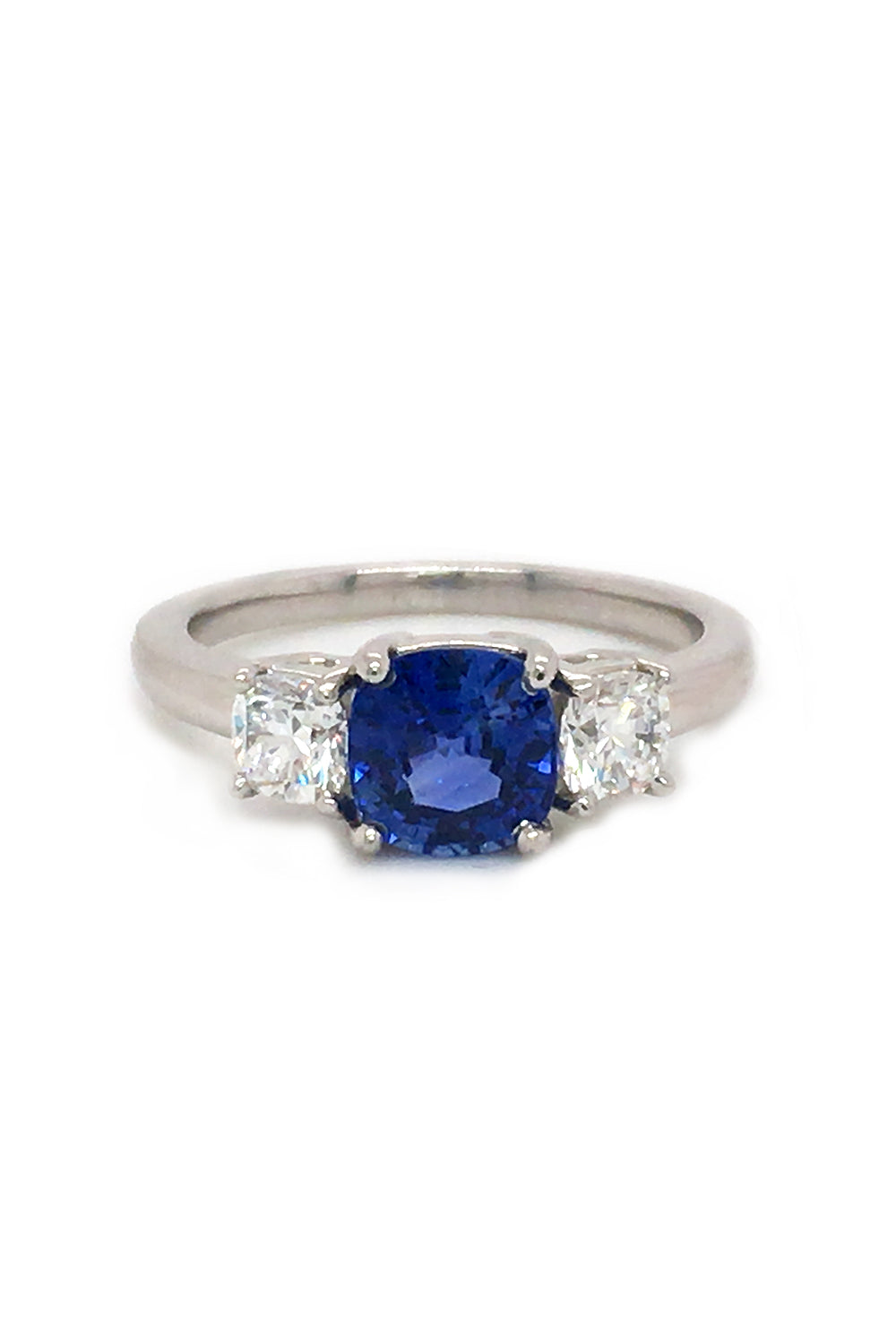 Angle view of platinum ring with blue sapphire and round diamonds on white background.