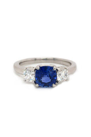 Angle view of platinum ring with blue sapphire and round diamonds on white background.