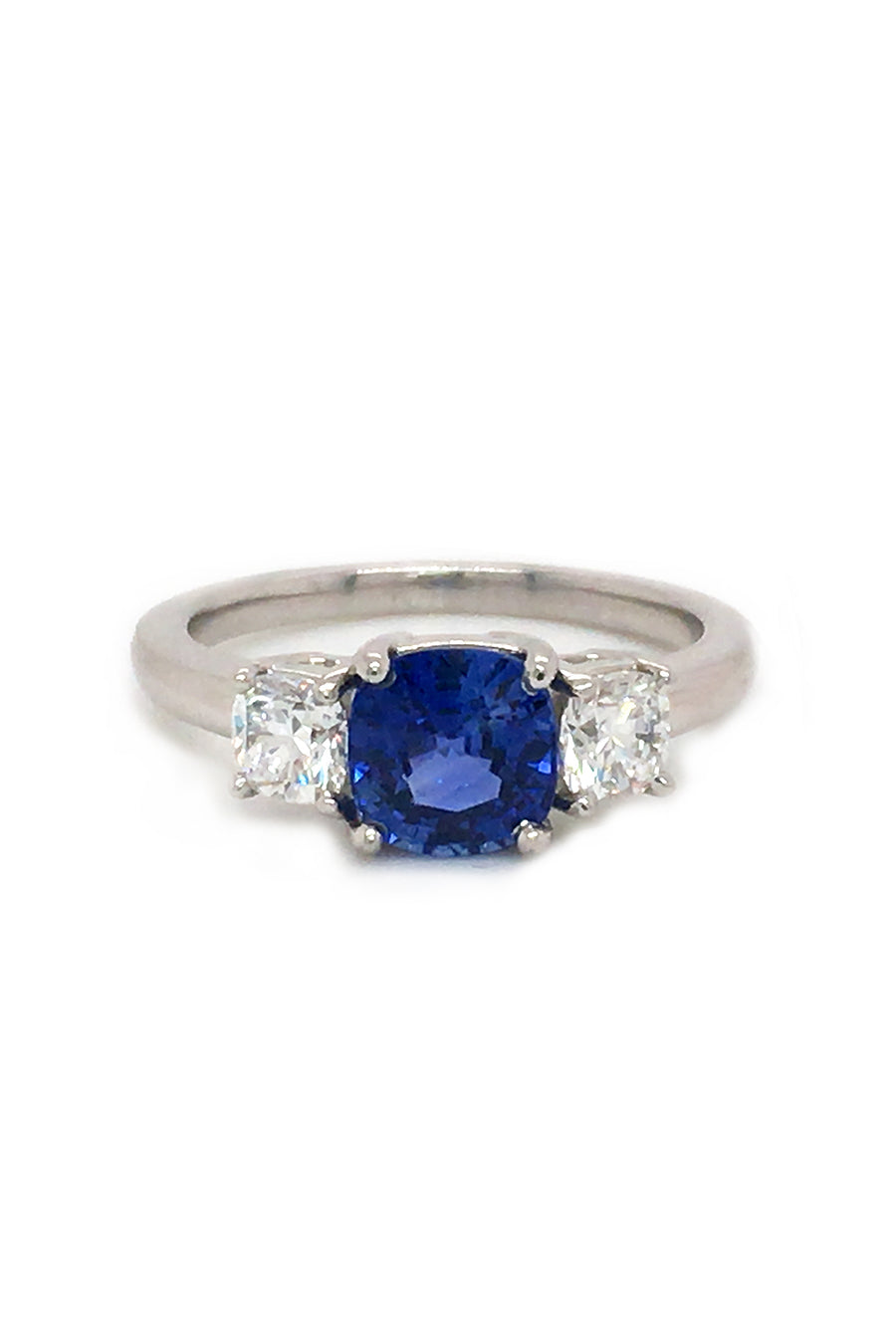 Angle view of platinum ring with blue sapphire and round diamonds on white background.
