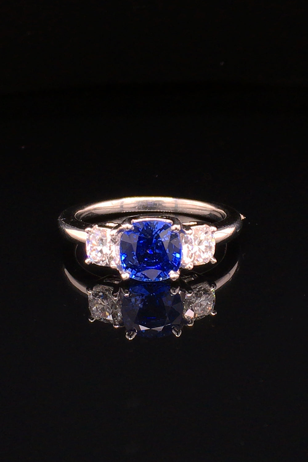 Platinum ring with blue sapphire and round diamonds on black background.