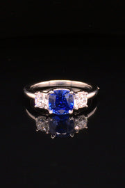 Platinum ring with blue sapphire and round diamonds on black background.