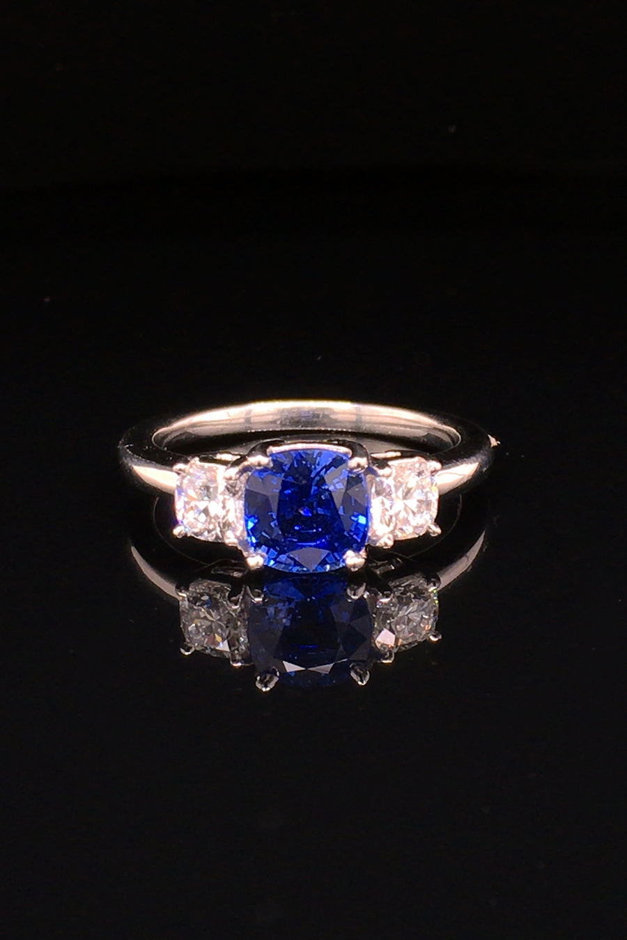 Platinum ring with blue sapphire and round diamonds on black background.