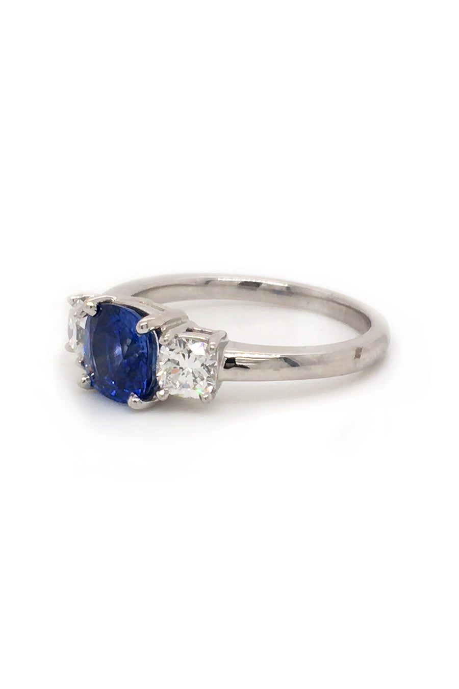 Angle view of platinum ring with blue sapphire and round diamonds on white background.