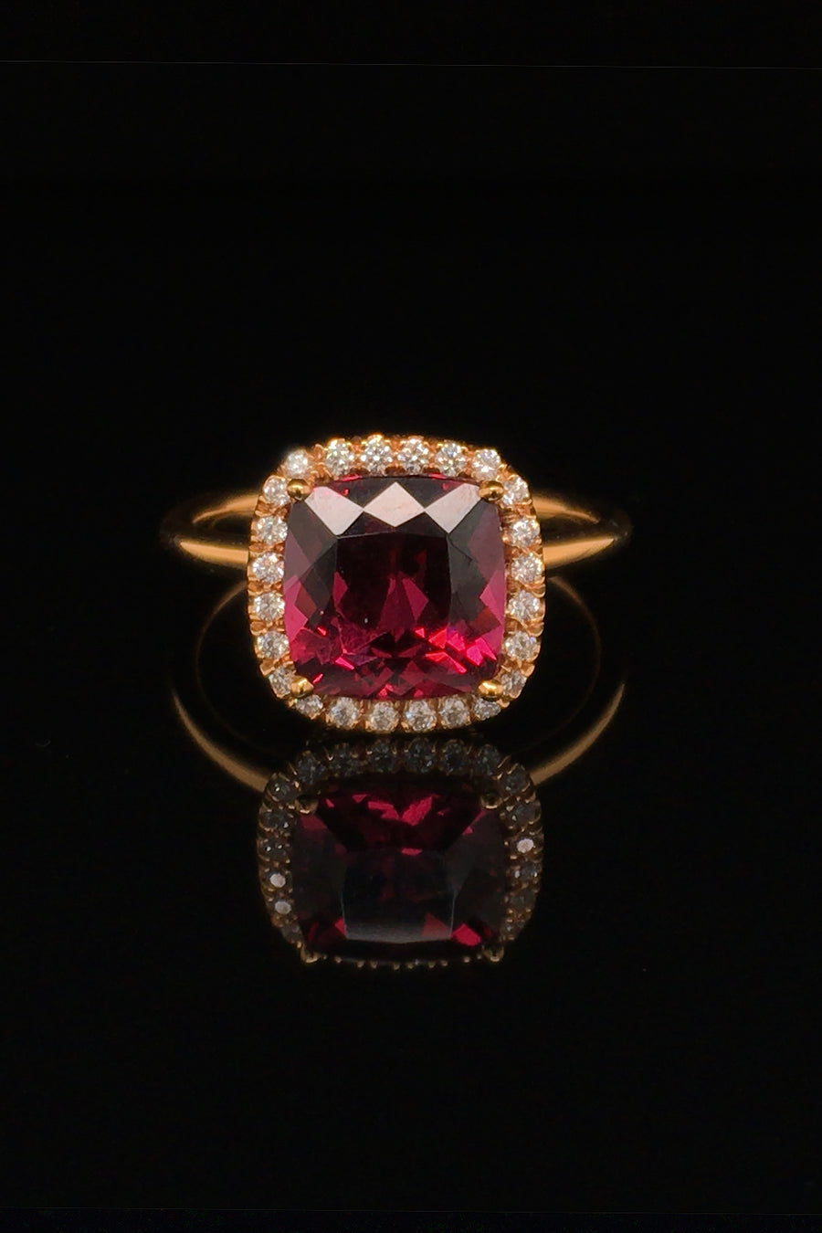 20K pink gold ring with a cushion-shaped rhodolite garnet and diamond halo on a black background.