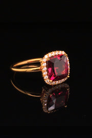 Side view of 20K pink gold ring with a cushion-shaped rhodolite garnet and diamond halo on a black background.